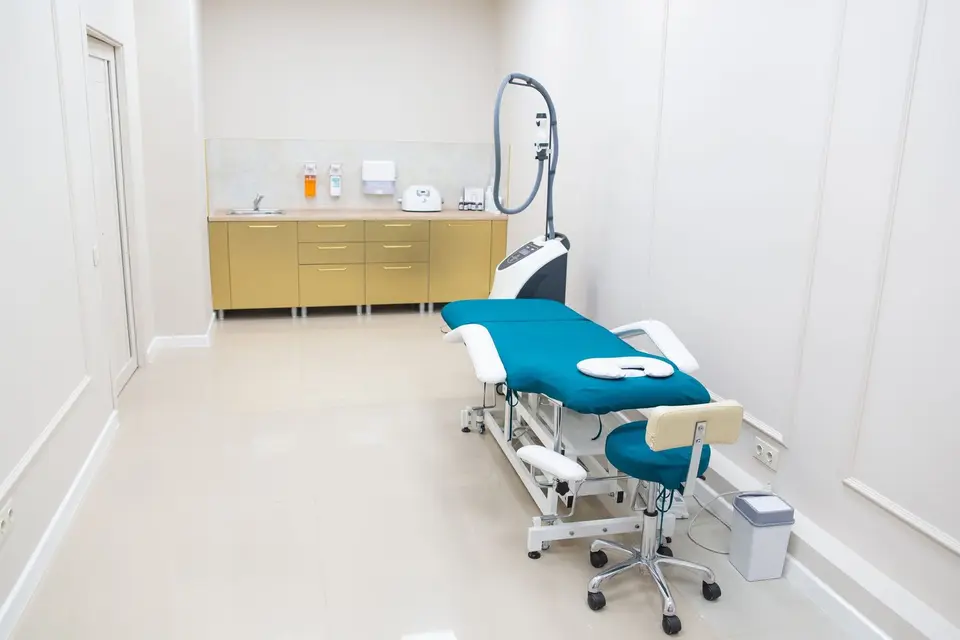 Sala de atendimento clara e vazia, com maca azul e bancada